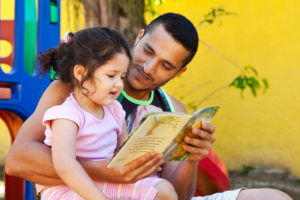 A father in Brazil reads a book to his daughter outside.